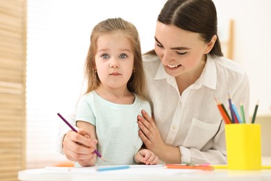 Mother and her little daughter drawing with colorful pencils at home