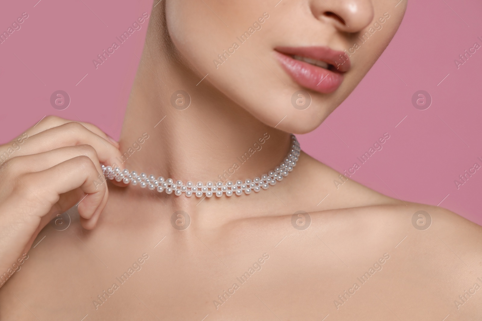 Photo of Young woman wearing elegant pearl necklace on pink background, closeup