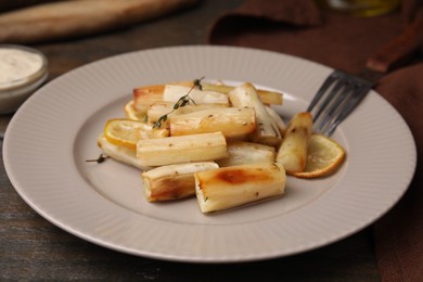 Photo of Plate with baked salsify roots, lemon, thyme and fork on wooden table, closeup
