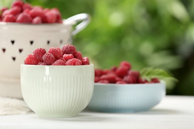 Photo of Different kitchenware with delicious ripe raspberries on white table against blurred background, space for text