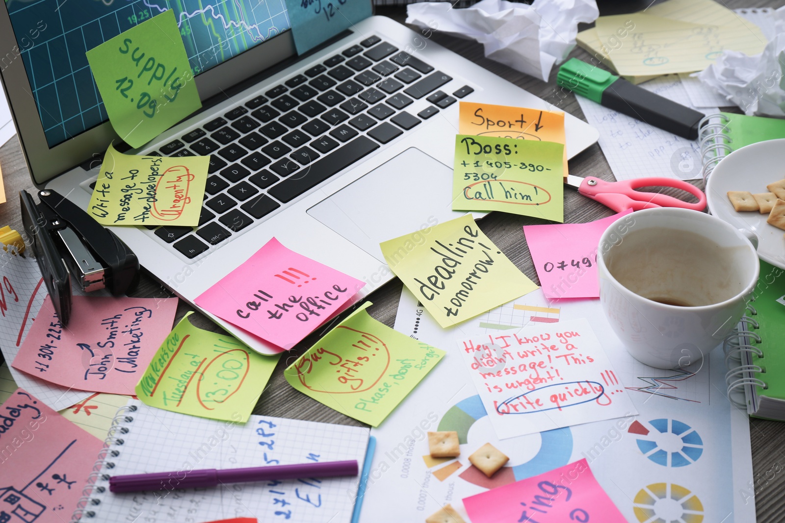 Photo of Laptop, notes and office stationery in mess on desk. Overwhelmed with work