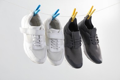 Photo of Different stylish sneakers drying on washing line against light grey background