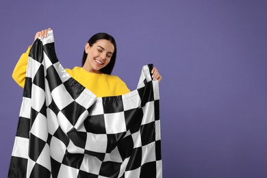 Photo of Happy young woman with checkered flag on violet background, space for text