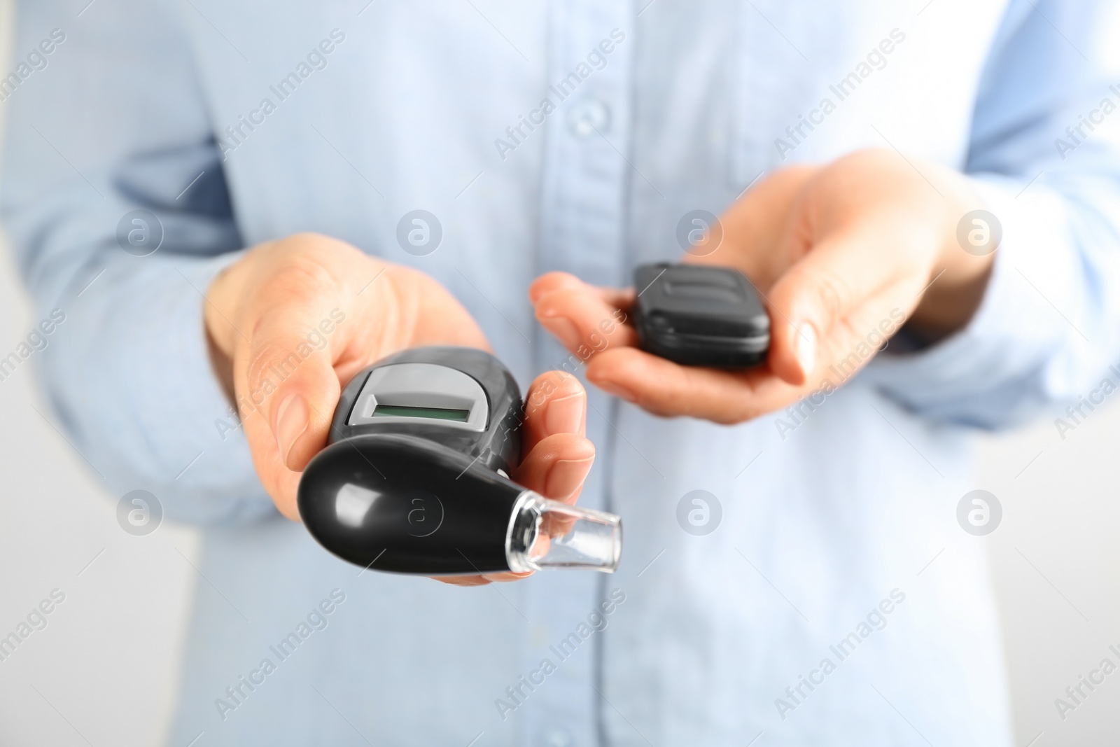 Photo of Woman holding modern breathalyzer and car key on light background, closeup