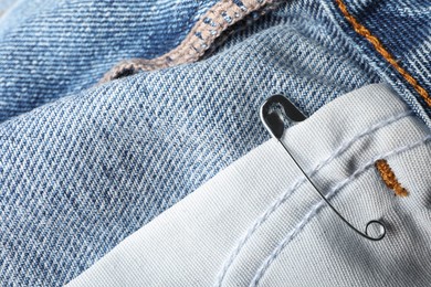 Metal safety pin on denim fabric, closeup