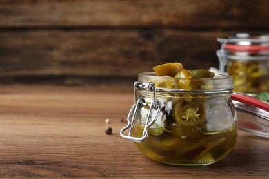 Photo of Glass jar with slices of pickled green jalapeno peppers on wooden table, space for text