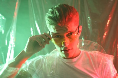 Photo of Stylish young man wearing clear coat and glasses in neon lights