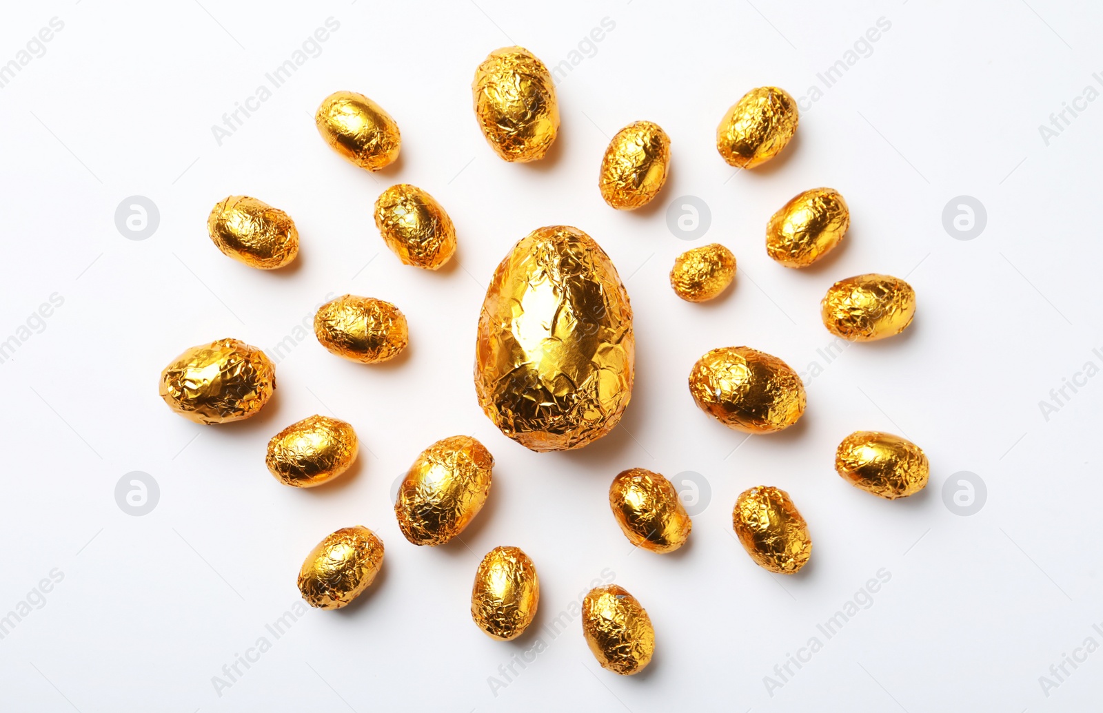 Photo of Chocolate eggs wrapped in golden foil on white background, flat lay