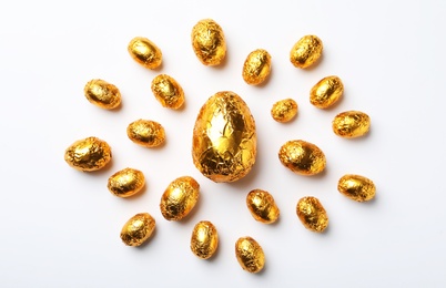 Photo of Chocolate eggs wrapped in golden foil on white background, flat lay