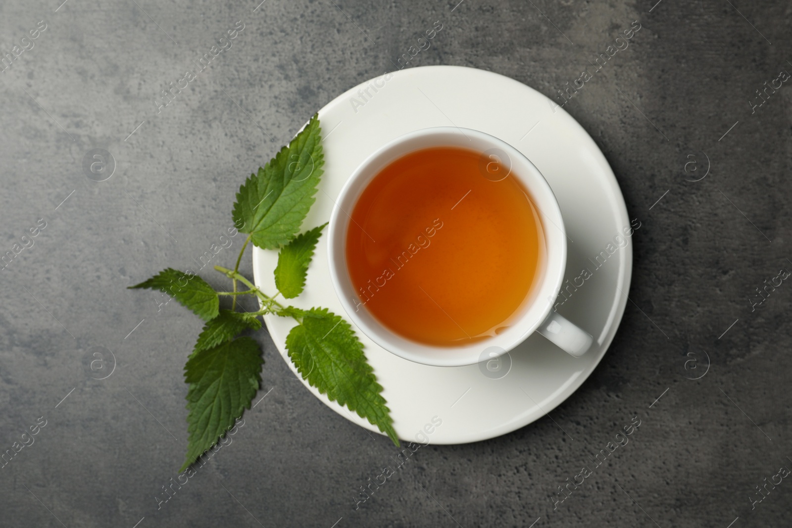 Photo of Cup of aromatic nettle tea and green leaves on grey table, top view