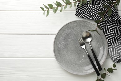 Photo of Stylish setting with cutlery, plate, napkin and eucalyptus branches on white wooden table, top view. Space for text