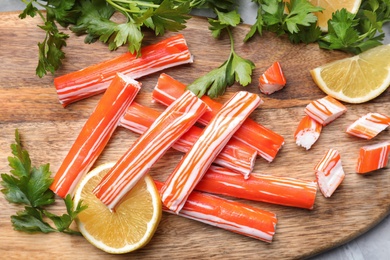 Photo of Delicious crab sticks with lemon slices and parsley on wooden board, flat lay