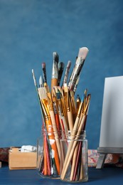 Many paintbrushes in glass jars on blue wooden table