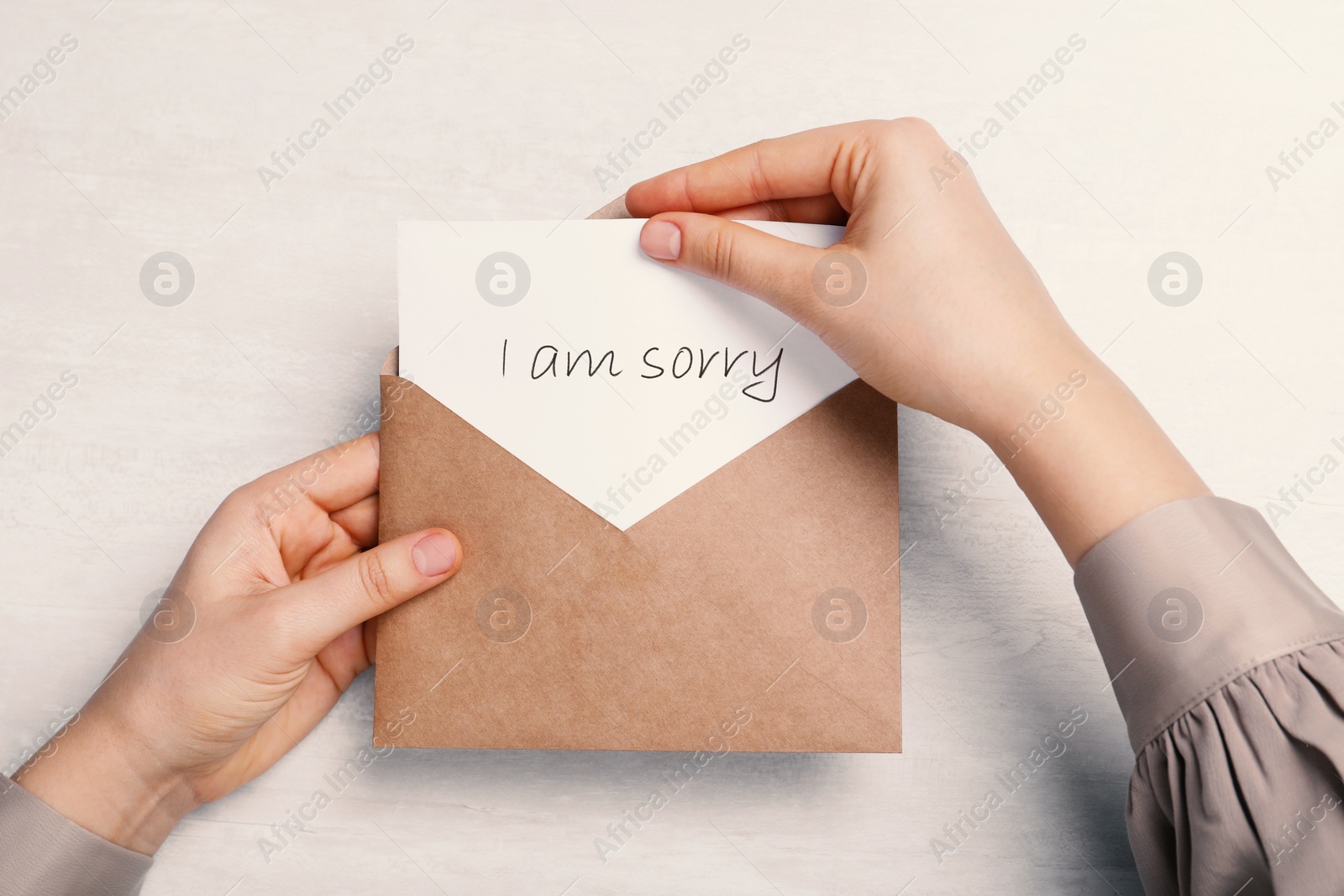 Image of Apology. Woman taking card with word Sorry out of envelope at light table, top view