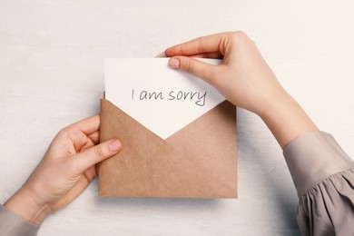 Apology. Woman taking card with word Sorry out of envelope at light table, top view