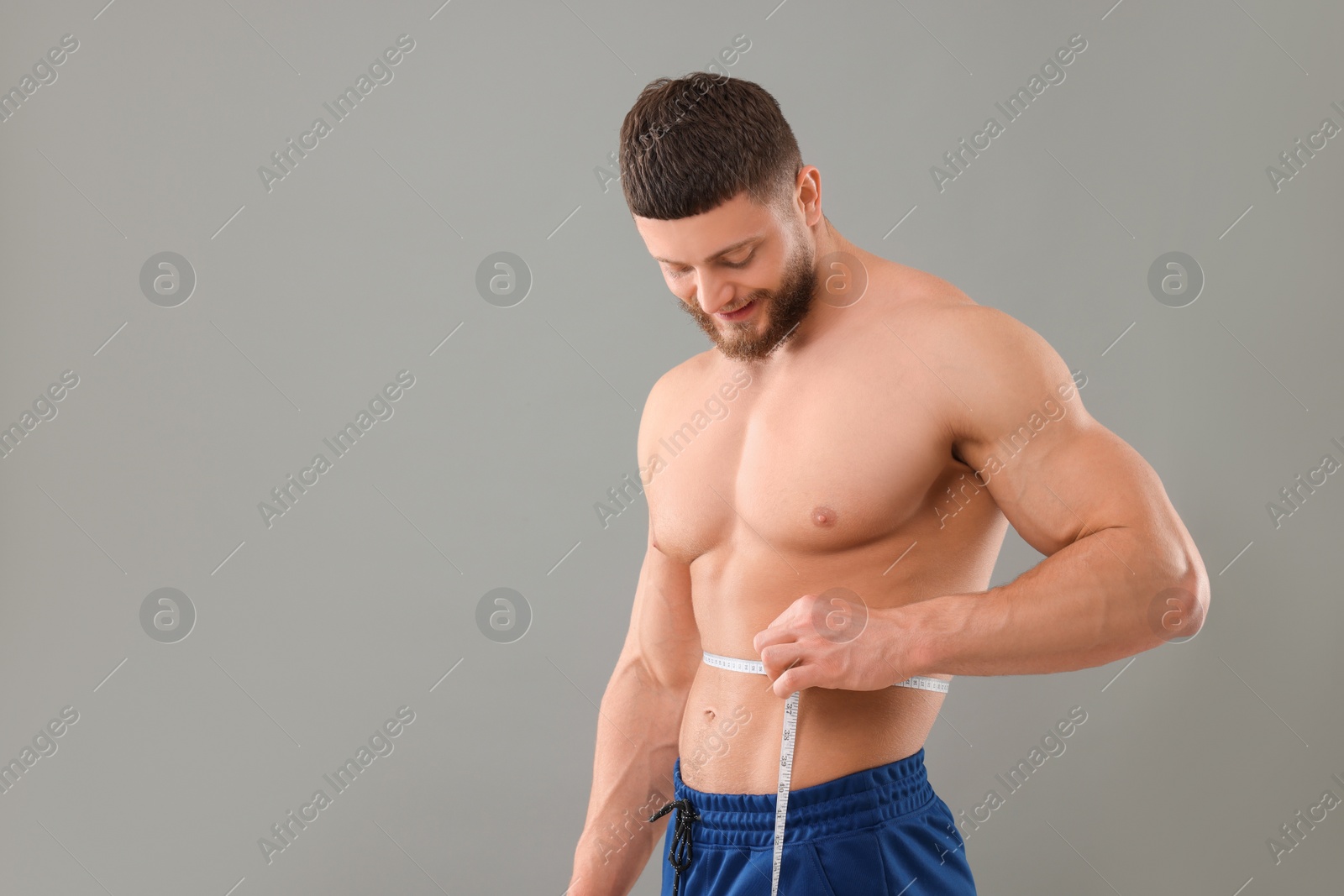 Photo of Athletic man measuring waist with tape on grey background, space for text. Weight loss concept