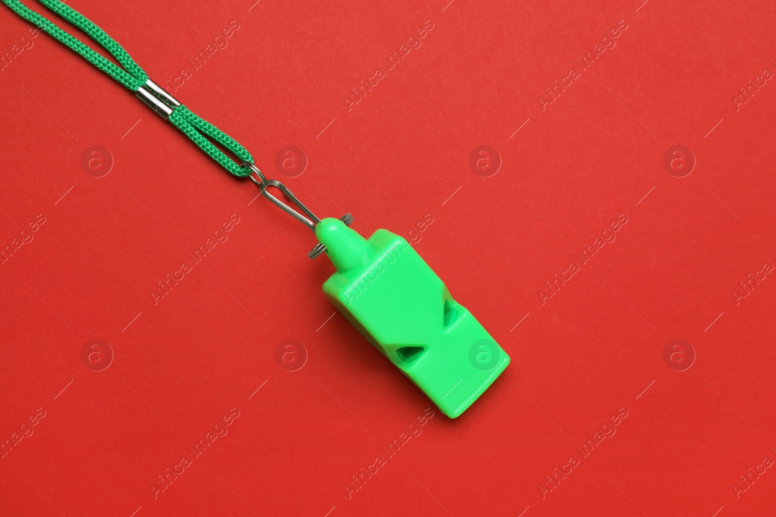 Photo of One green whistle with cord on red background, top view