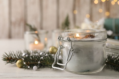 Photo of Burning scented conifer candle and Christmas decor on white wooden table. Space for text