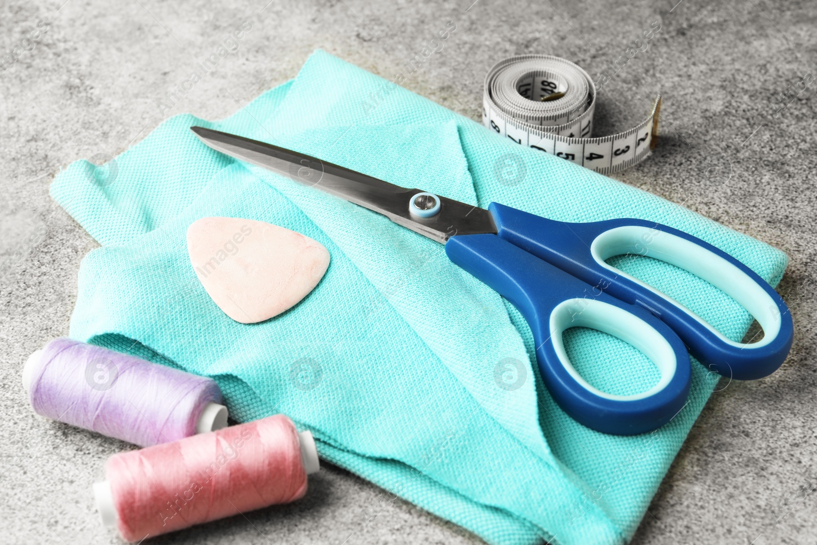 Photo of Scissors, spools of threads and sewing tools on grey background, closeup