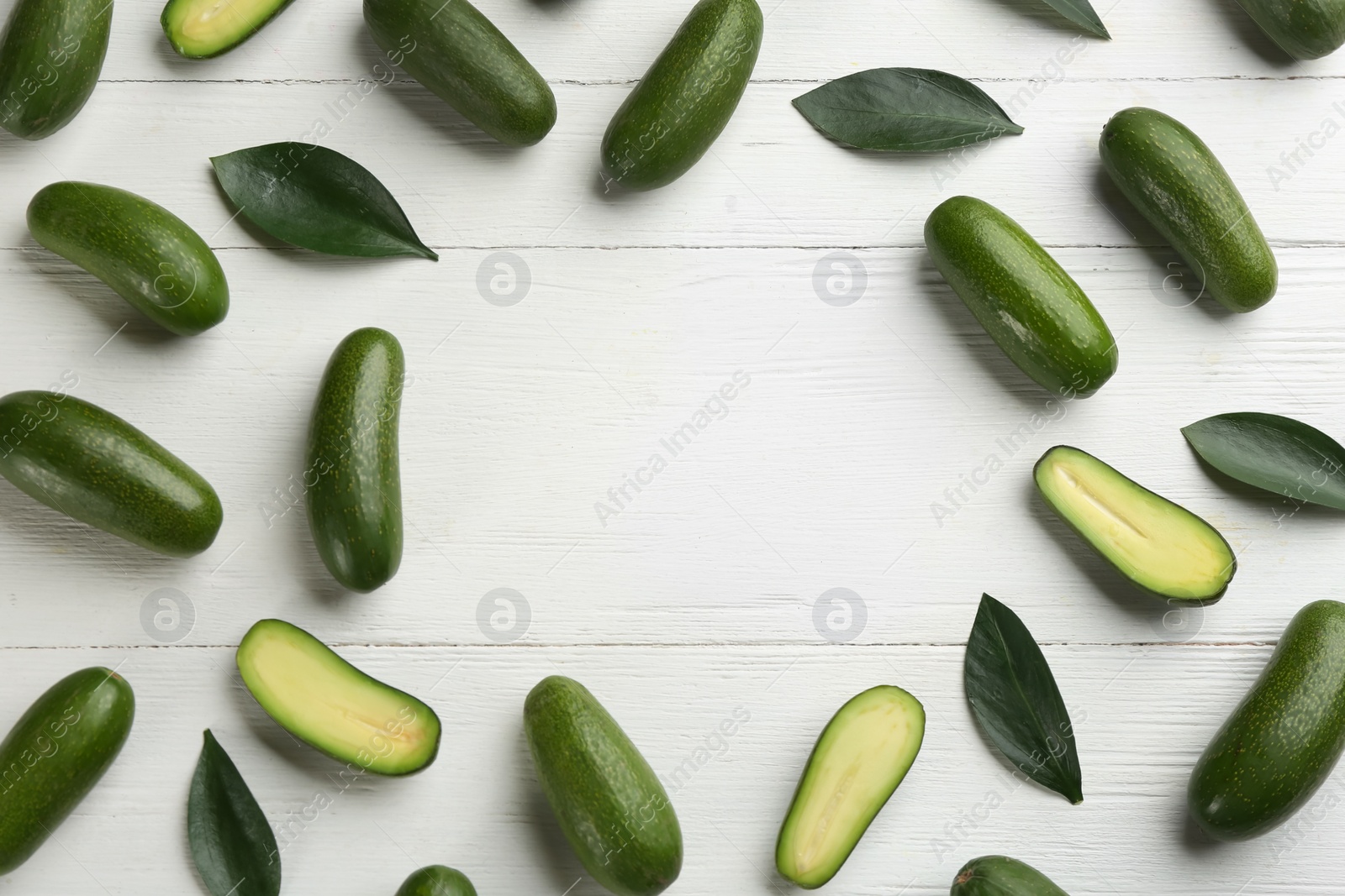 Photo of Frame made of fresh seedless avocados with green leaves on white wooden table, flat lay. Space for text