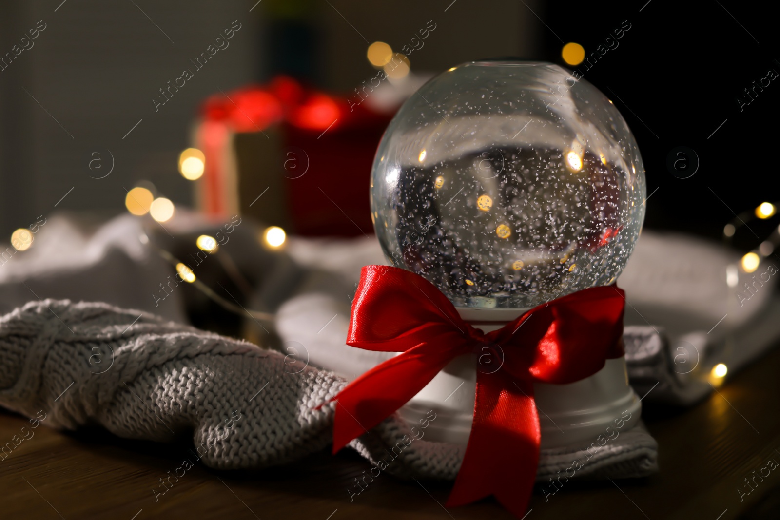 Photo of Christmas snow globe with knitting sweater on wooden table. Space for text