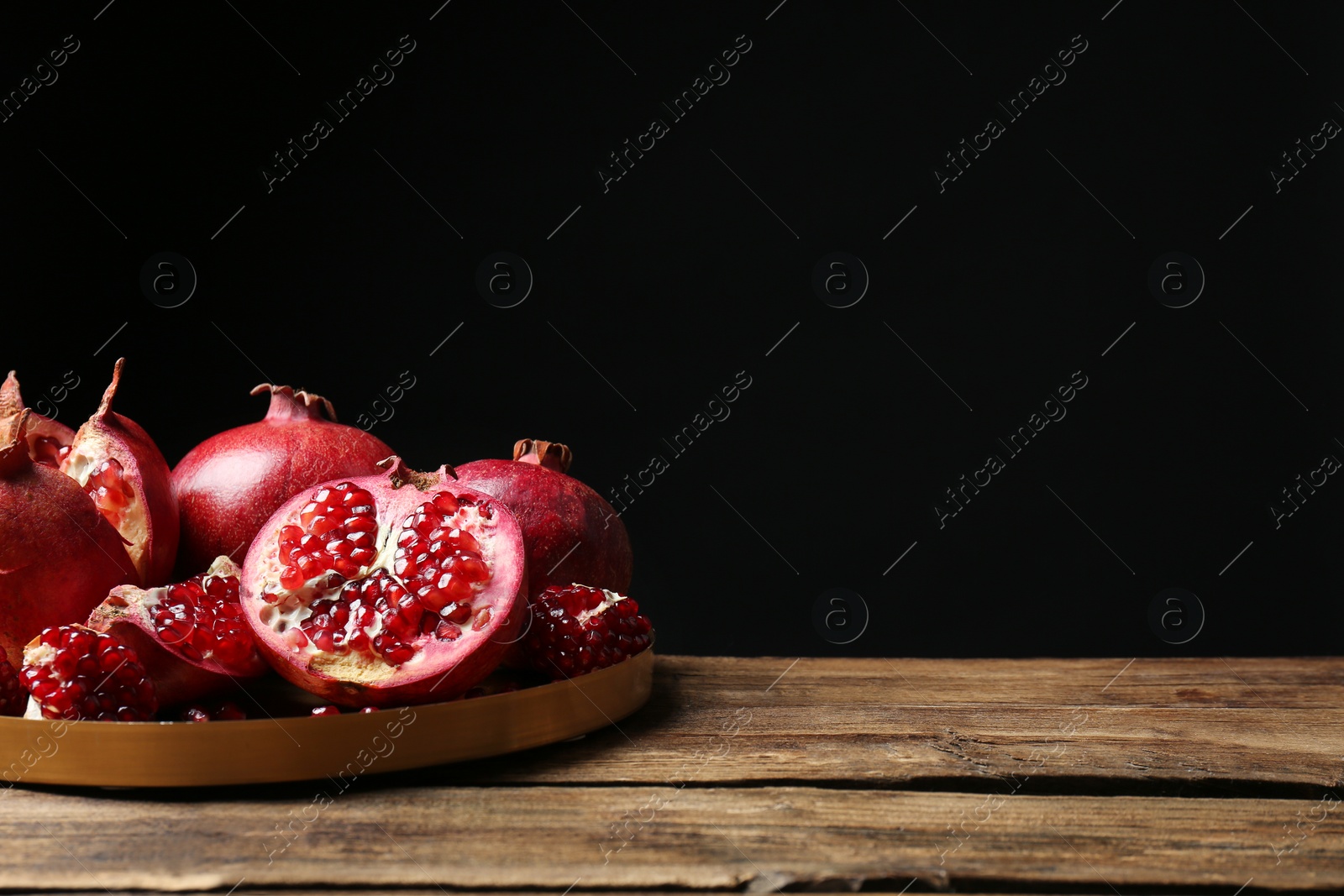 Photo of Tray with ripe pomegranates on table against black background, space for text