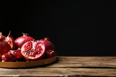 Photo of Tray with ripe pomegranates on table against black background, space for text