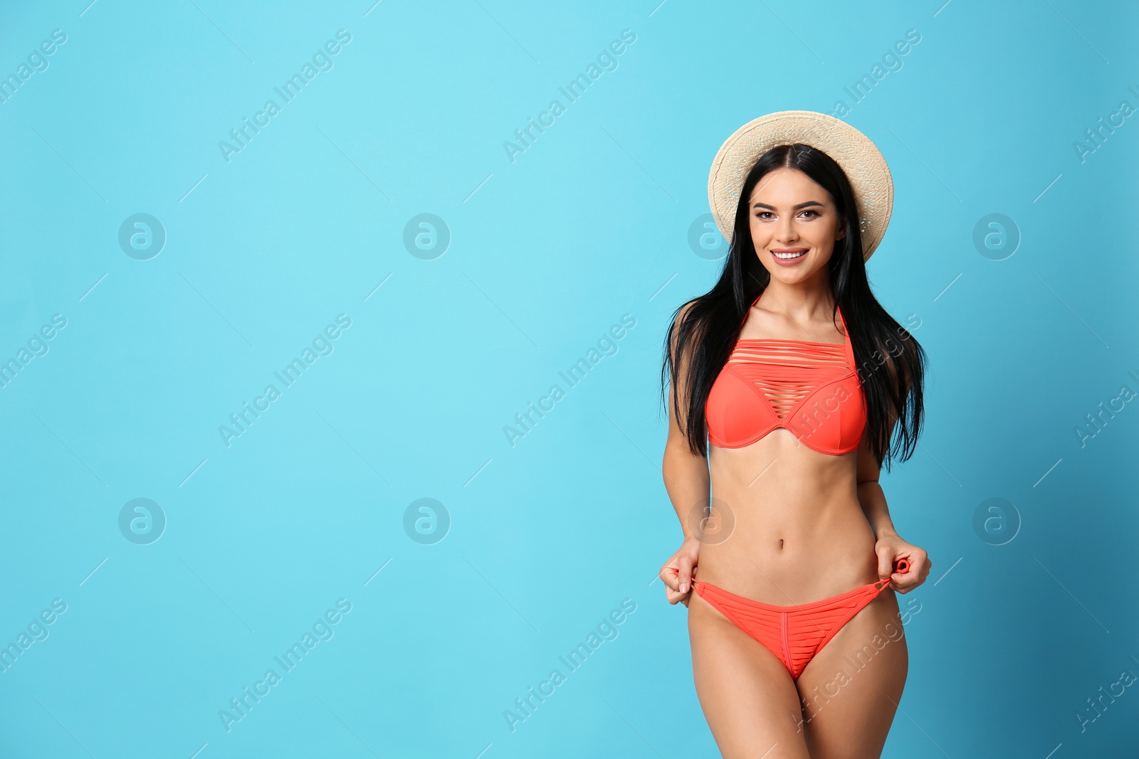 Photo of Beautiful young woman in stylish bikini with hat on light blue background. Space for text