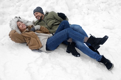 Photo of Happy couple lying on snow outdoors. Winter vacation