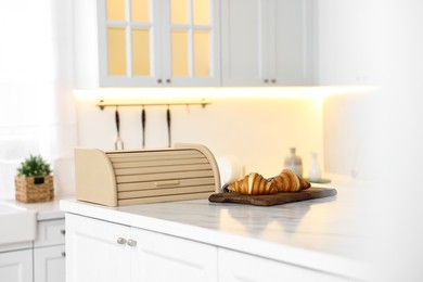 Wooden bread box and board with croissants on white marble countertop in kitchen