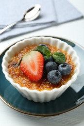 Photo of Delicious creme brulee with berries and mint in bowl on white wooden table, closeup