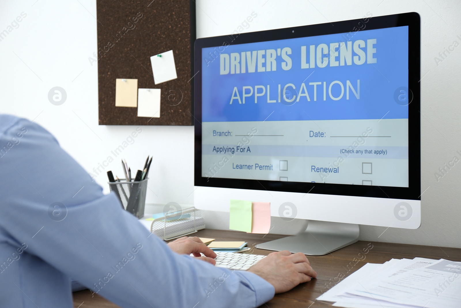 Photo of Man using computer to fill driver's license application form at table in office, closeup