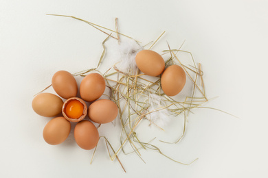 Photo of Raw chicken eggs and decorative straw on white table, flat lay