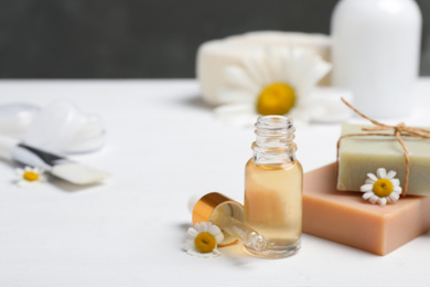 Composition with chamomile flowers and cosmetic products on white wooden table, space for text