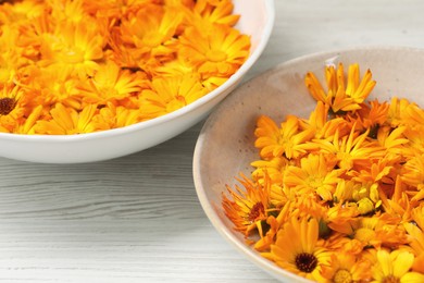 Photo of Beautiful calendula flowers in bowls on white wooden table, closeup