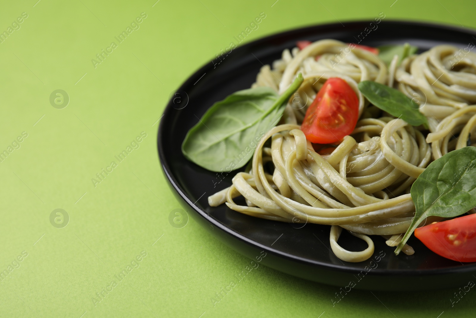 Photo of Tasty pasta with spinach, sauce and tomatoes on green table, closeup. Space for text