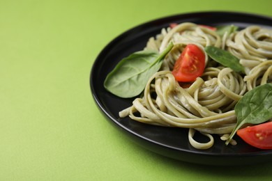 Photo of Tasty pasta with spinach, sauce and tomatoes on green table, closeup. Space for text