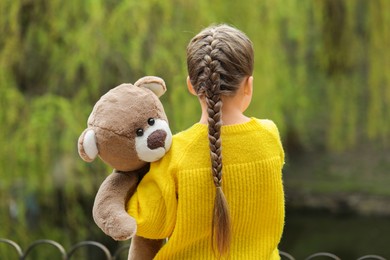 Photo of Little girl with teddy bear outdoors, back view