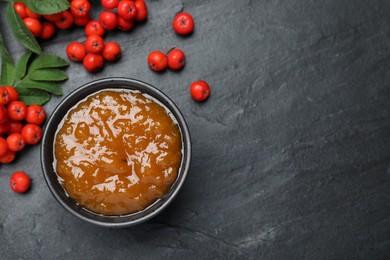 Photo of Delicious rowan jam in bowl and berries on dark table, flat lay. Space for text