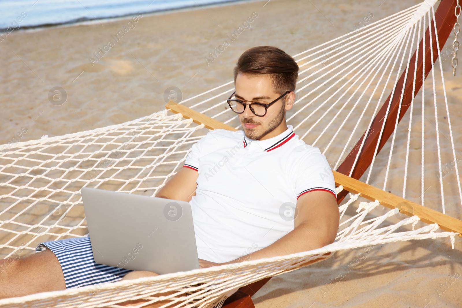 Photo of Young man with laptop resting in hammock at seaside