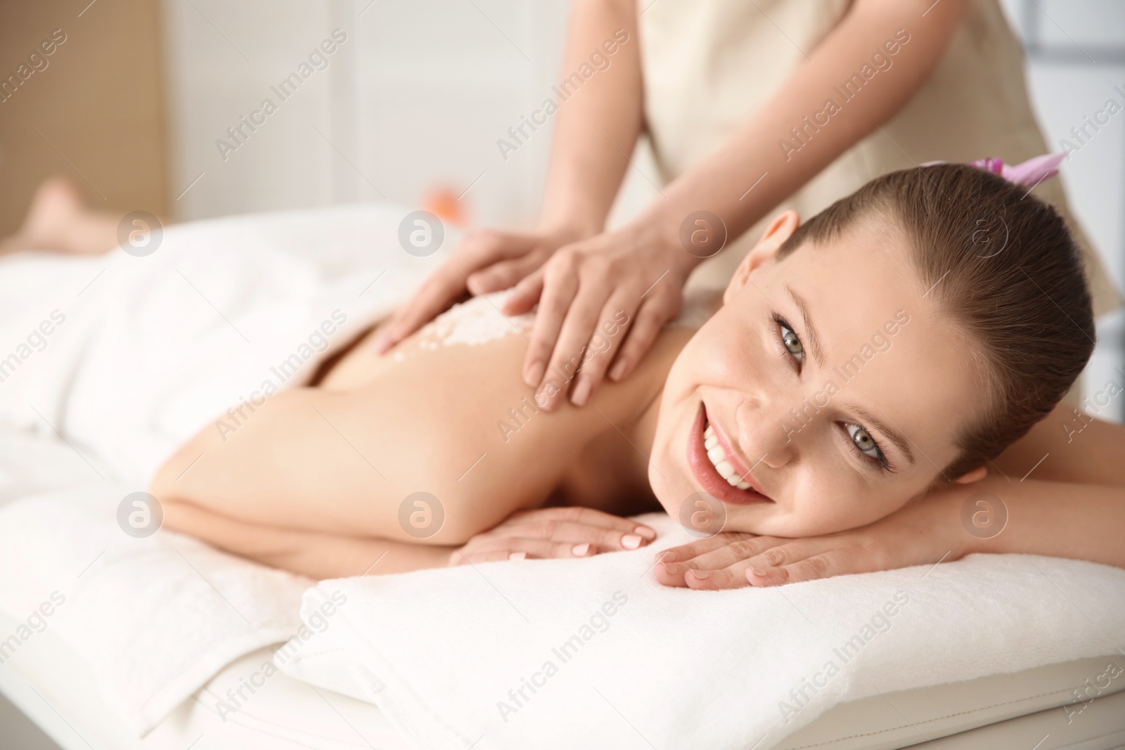 Photo of Beautiful young woman having massage with body scrub in spa salon