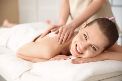 Beautiful young woman having massage with body scrub in spa salon