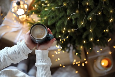 Photo of Woman holding cup of cocoa near Christmas tree indoors, above view