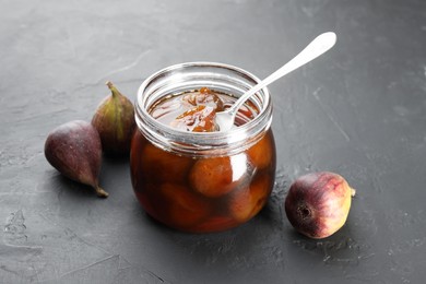 Photo of Jar of tasty sweet jam and fresh figs on black table