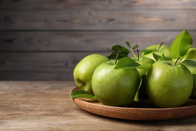 Photo of Fresh ripe green apples and leaves with plate on wooden table. Space for text
