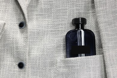 Photo of Luxury men's perfume in pocket of grey jacket, top view. Space for text