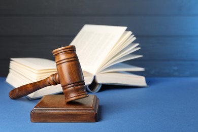 Photo of Wooden gavel, sound block and book on blue table, closeup. Space for text