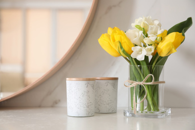 Photo of Beautiful yellow tulips and freesia flowers near mirror on white table, space for text