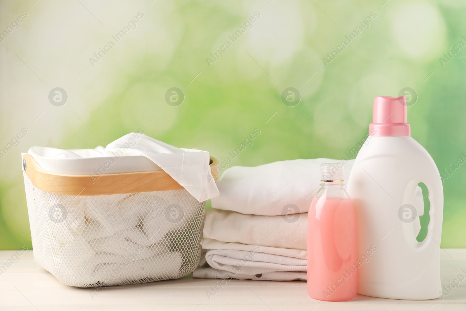 Photo of Bottles of laundry detergents and clean clothes on white wooden table