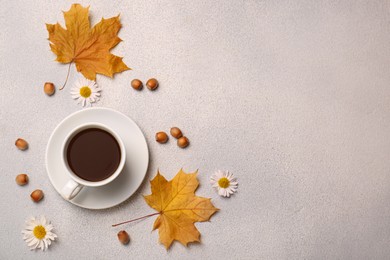 Flat lay composition with cup of hot drink and autumn leaves on light grey textured table. Space for text